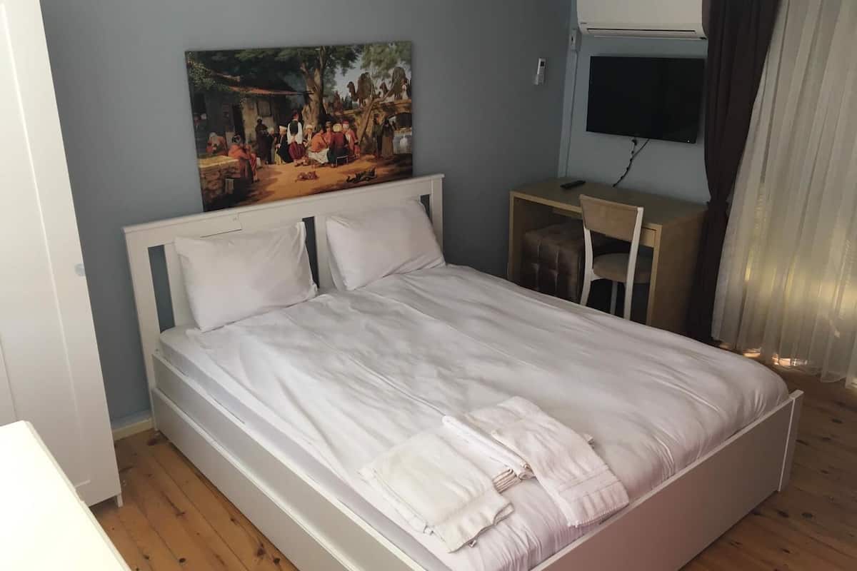 A bedroom with a bed, a desk, and a painting on the wall.