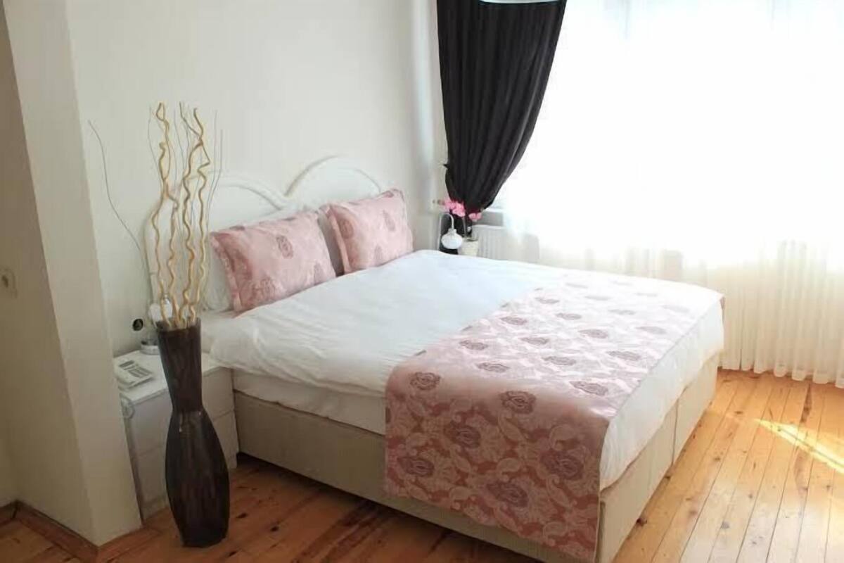 A bedroom with a bed, a nightstand, a vase with branches, and a window with curtains.