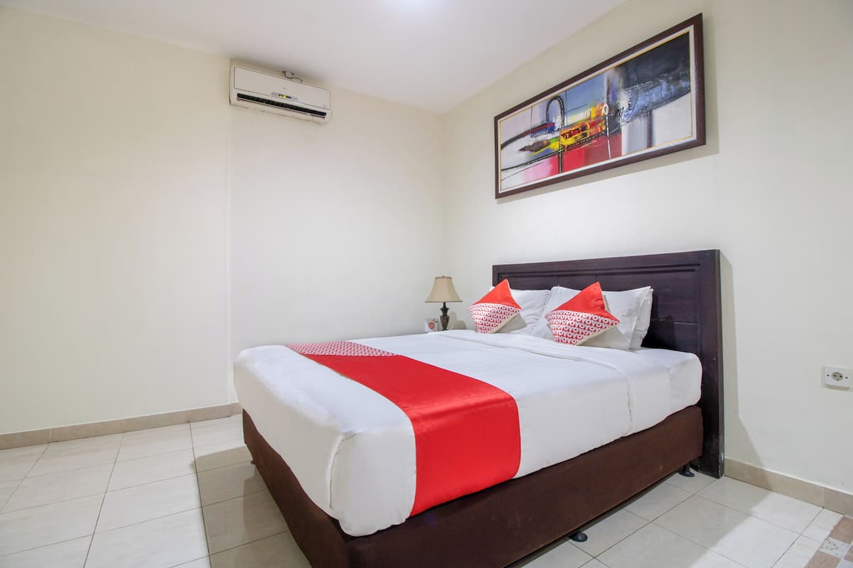 Un lit bien fait, recouvert d’une couvre-lit rouge et blanche, avec une tête de lit sombre et un climatiseur fixé au mur.