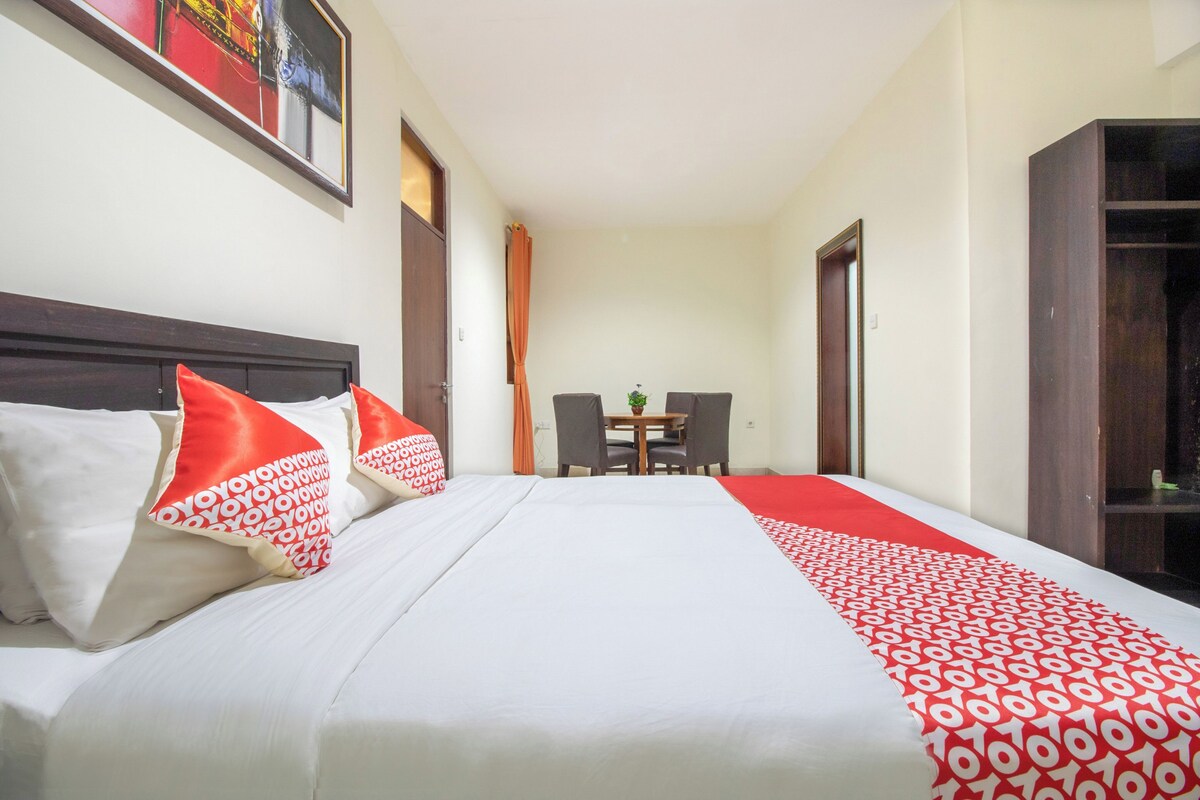 A hotel room with a large bed, a wooden headboard, a dining table with chairs, and a wardrobe.