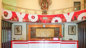 Un espace d’accueil avec un bureau rouge et blanc, une horloge et un mur décoratif orné d’une fresque représentant un paysage urbain.