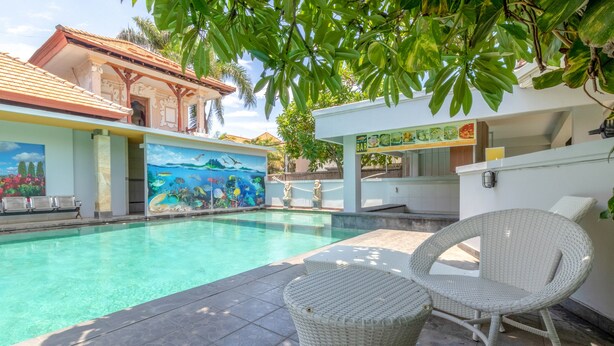 Une piscine ornée d’une fresque murale, des meubles en osier et un coin bar.