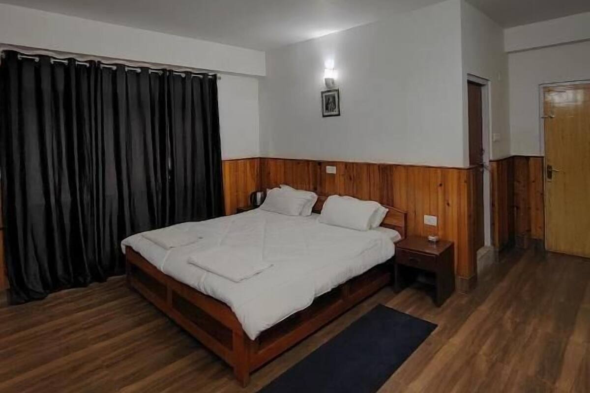 A bedroom with a wooden bed, a nightstand, a black rug, a wooden door, and a black curtain.