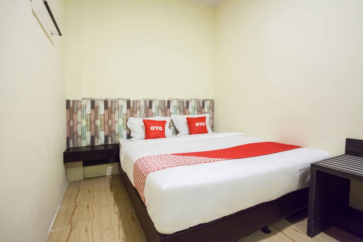 A hotel room with a bed, a nightstand, a table, and a wall with a decorative panel.