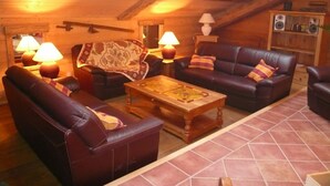 A cozy log cabin interior with a fireplace, leather sofas, and a wooden coffee table.
