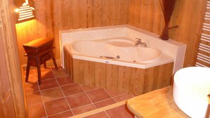 A wooden bathroom with a large bathtub, a wooden bench, and a tiled floor.