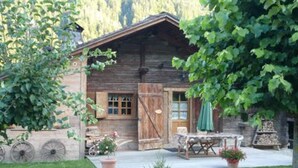 A rustic wooden cabin with a porch, a table, and chairs.