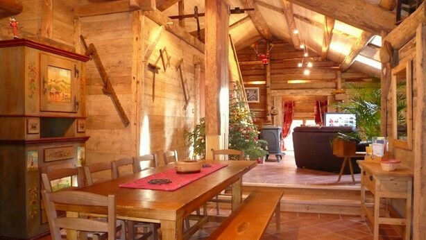 A rustic wooden cabin interior with a dining table, benches, and a fireplace.
