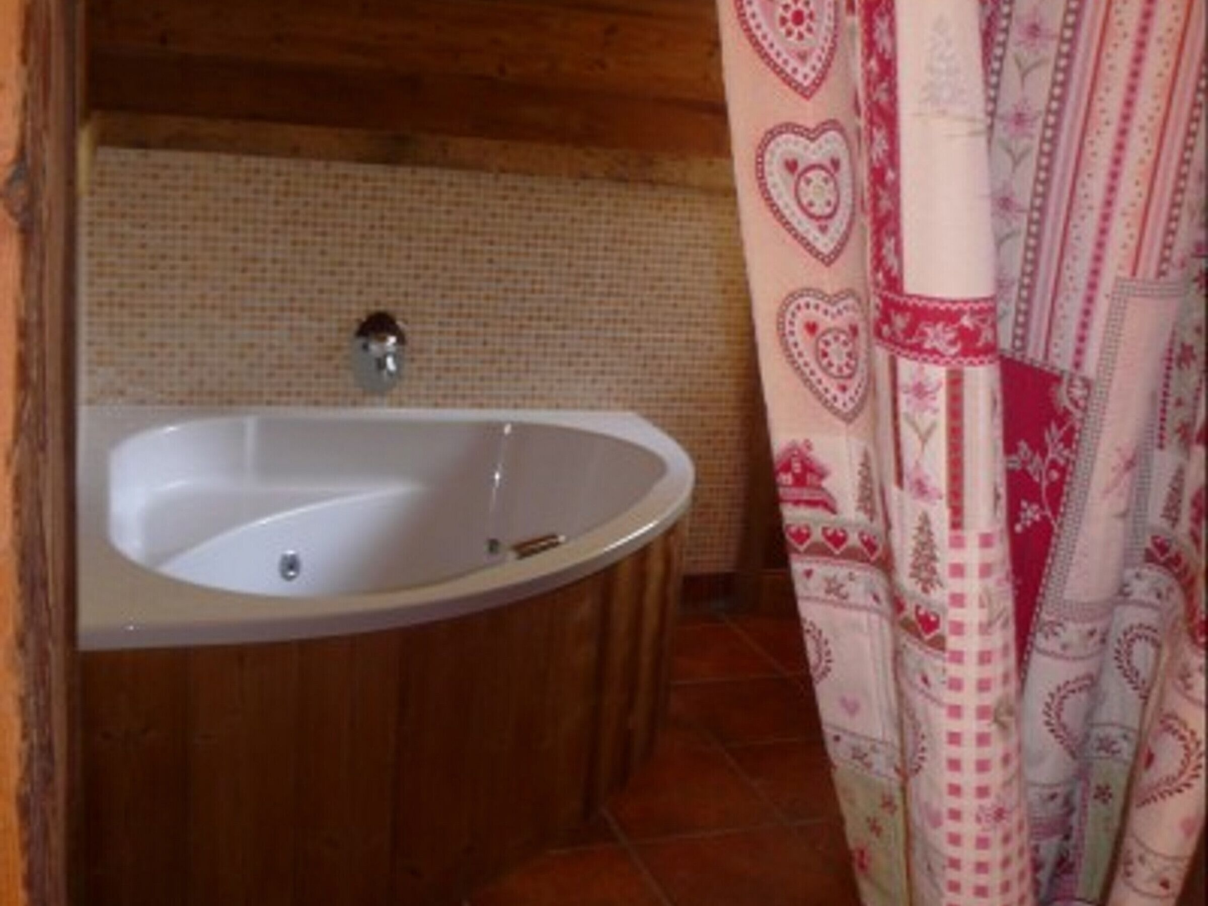 Een badkamer met een wit bad, een betegelde muur en een douchegordijn met patroon.