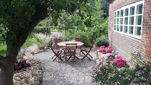 Un patio jardín con mesa y sillas de madera, rodeado de grava y plantas en flor.
