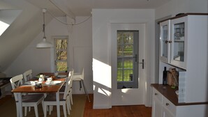 Un comedor con una mesa de madera y sillas blancas, una ventana con vistas a zonas verdes y un armario blanco con puertas de cristal.