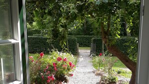 Un sendero en un jardín que lleva a una puerta, rodeado de follaje y flores.