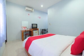 Quarto de hotel com cama, escrivaninha com computador, pequeno frigorífico e televisão.