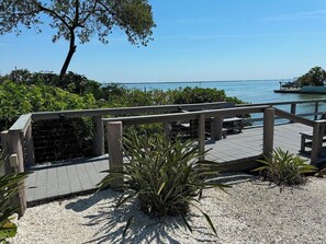 A wooden deck with a railing overlooking a body of water, surrounded by greenery and a clear sky. - Weekly / Monthly Rental - Spacious Condo IN Longboat Key Resort Close TO Pool, Tennis And Beach! (Longboat Key)