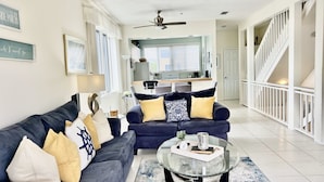 A modern living room with a dark blue sofa, a glass coffee table, and a staircase leading to an upper level. - Weekly / Monthly Rental - Spacious Condo IN Longboat Key Resort Close TO Pool, Tennis And Beach! (Longboat Key)