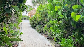 A pathway flanked by lush greenery and a thatched-roof structure in the distance. - Weekly / Monthly Rental - Spacious Condo IN Longboat Key Resort Close TO Pool, Tennis And Beach! (Longboat Key)