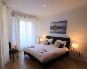 Une chambre d’hôtel avec un grand lit, deux lampes de chevet, un tableau au mur et une chaise.