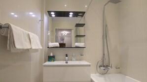 A modern bathroom with a bathtub, a shower, a sink with a mirror above it, and a towel rack with towels. - Libération (Nice)