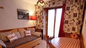 A cozy room with a wooden sofa, a dining table with a checkered tablecloth, and patterned curtains. - Cozy 1BR with terrace in Arêches, sleeps 4, near slopes and shuttle (Arêches-Beaufort)