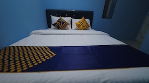 A bed with a white and blue bedspread, two pillows with yellow and blue patterns, and a dark headboard. - OYO 2302 Blue House Costel Syariah (Cianjur)
