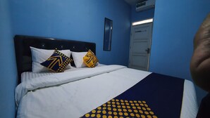 A bed with white bedding and two decorative pillows, a dark headboard, and a blue wall. - OYO 2302 Blue House Costel Syariah (Cianjur)