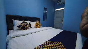 A bed with white bedding and two decorative pillows, a dark headboard, and a blue wall.