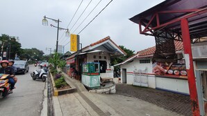 A street view with a small building that appears to be a restaurant or cafe, with outdoor seating and a sign advertising 'Roti Bakar & Kuku'. - OYO 2302 Blue House Costel Syariah (Cianjur)