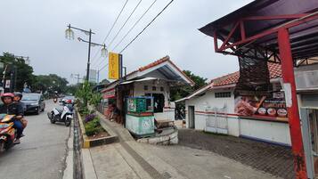 A street view with a small building that appears to be a restaurant or cafe, with outdoor seating and a sign advertising 'Roti Bakar & Kuku'.
