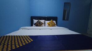 A bed with white bedding, two decorative pillows with geometric patterns, a blue wall, and a mirror on the wall.