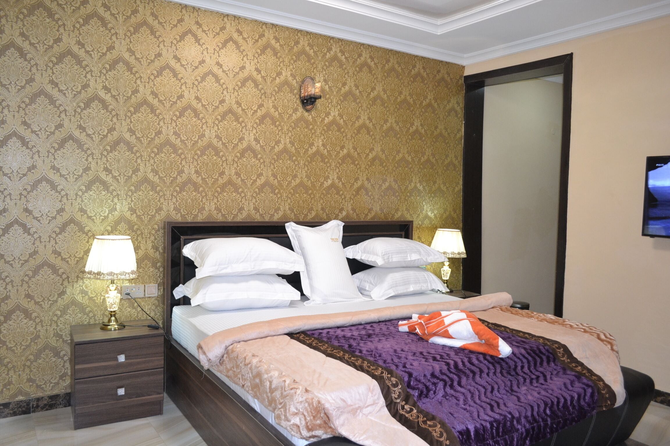 Hotelkamer met een groot bed, twee nachtkastjes met lampen, een tv aan de muur en behang met een patroon.