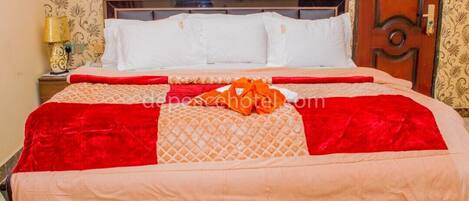 Una cama bien tendida con una colcha rojo y beig, un cabecero de madera y un papel tapiz estampado.