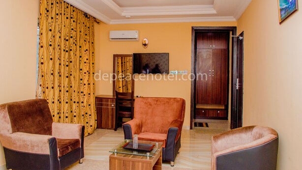 A living room with two armchairs, a sofa, a glass coffee table, a television, and a wooden cabinet. - Peace Hotel and Suites (Ilorin)