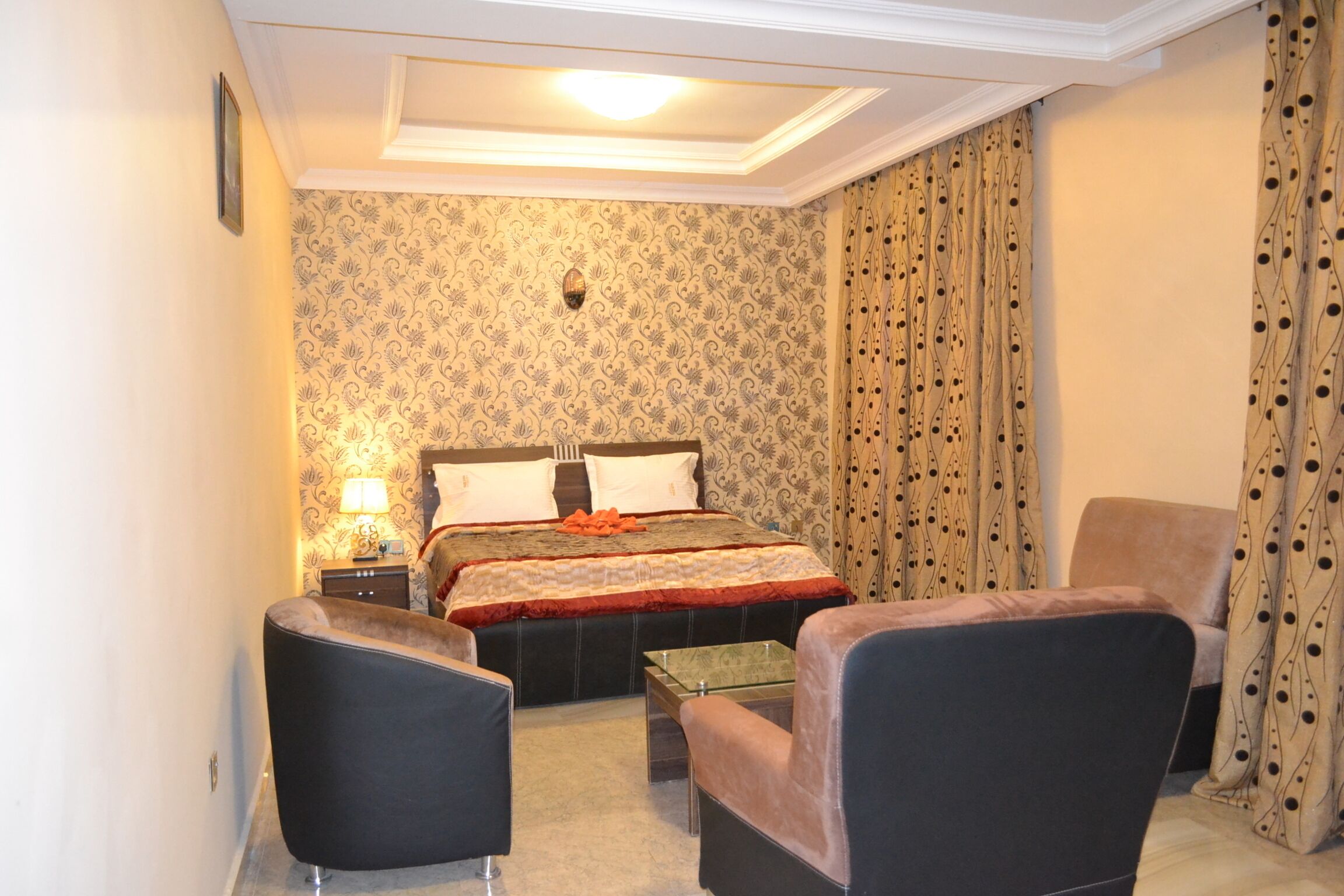 Habitación de hotel con una cama, dos sillones, una mesita y una mesita de noche con lámpara.
