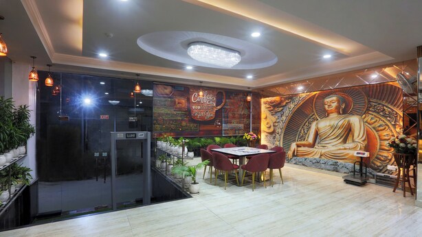 A modern interior with a Buddha mural, a coffee-themed wall, and a dining area with red chairs. - Castle Blue By Excellent Hospitality (New Delhi)