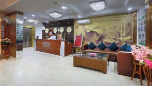 A hotel reception area with a reception desk, a sofa, a coffee table, and a wall with a mural. - Castle Blue By Excellent Hospitality (New Delhi)
