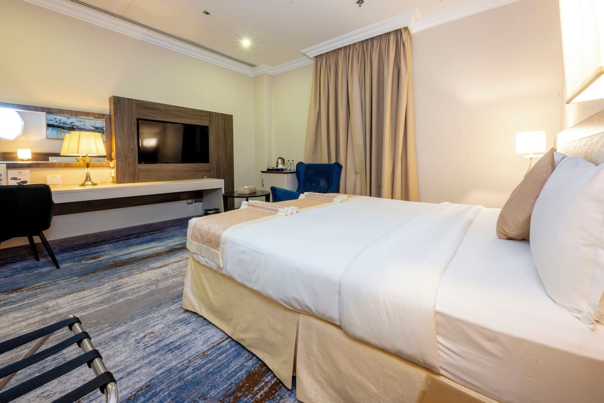 Habitación de hotel con una cama grande, un escritorio con lámpara, un televisor y una silla.