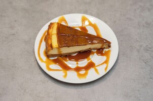 Una porción de pastel de queso con salsa de caramelo sobre un plato blanco.