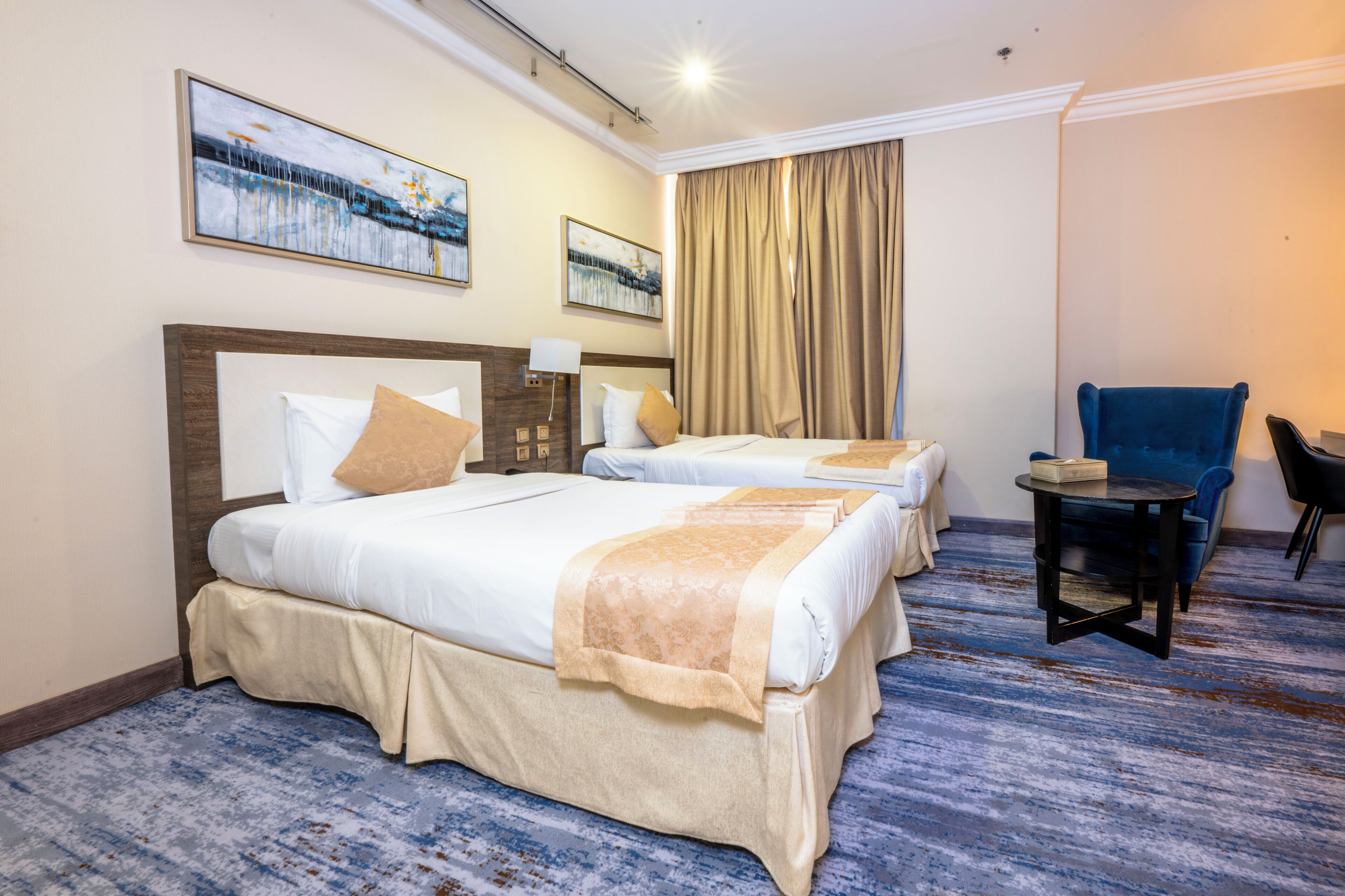 Een hotelkamer met twee bedden, een kleine tafel, een stoel en kunstwerken aan de wanden.