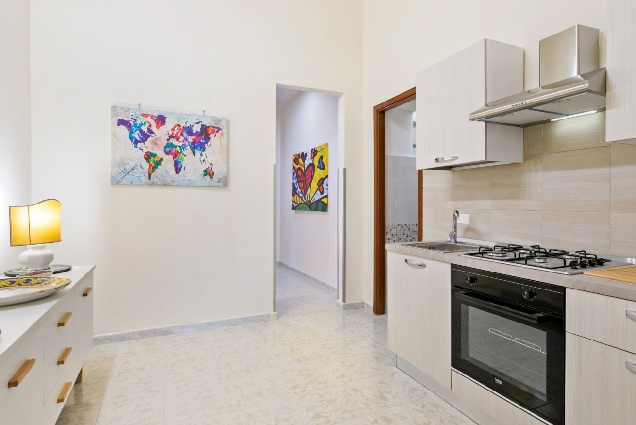 A modern kitchen with a gas stove, oven, and white cabinetry. There is a world map artwork on the wall and a lamp on the left.