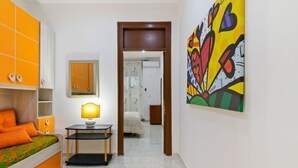 Un dormitorio con cama, mesita de noche, lámpara y un cuadro de colores en la pared.
