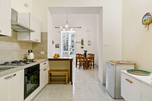 A modern kitchen with a gas stove, oven, and a small refrigerator. There is a dining area with a wooden table and chairs, and a bench.