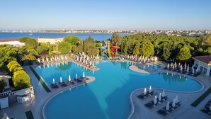 Uma grande piscina ao ar livre com várias pistas e um tobogã, rodeada por espreguiçadeiras e guarda-sóis.