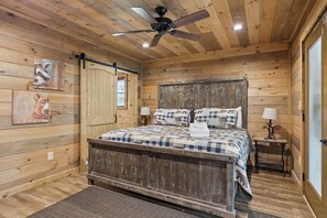 Dormitorio de cabaña de madera con cama, ventilador de techo, obras de arte y mesita de noche.