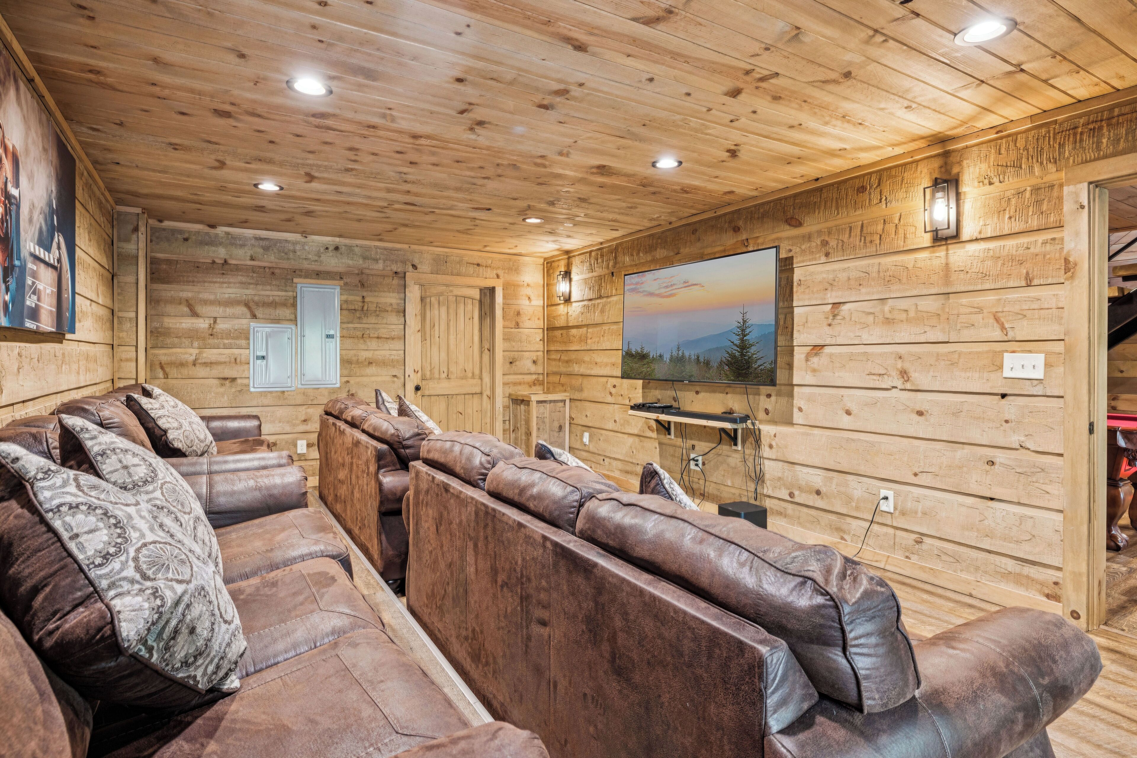A wooden-paneled room with a leather sofa, a flat-screen TV mounted on the wall, and a door leading to another area.