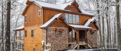 A multi-story wooden cabin with a stone foundation, large windows, and a covered porch.