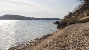Een kiezelstrand met helder water en een verre heuvel.