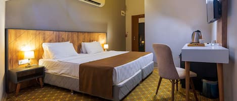 Una habitación de hotel con cama, mesitas de noche, escritorio, silla, equipo de aire acondicionado, televisor y piso con estampado.