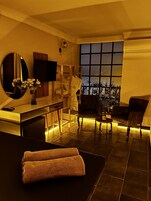 Una habitación de hotel moderna con un ventanal grande, un televisor de pantalla plana, un escritorio de madera, una silla y una mesa de masajes con toallas.