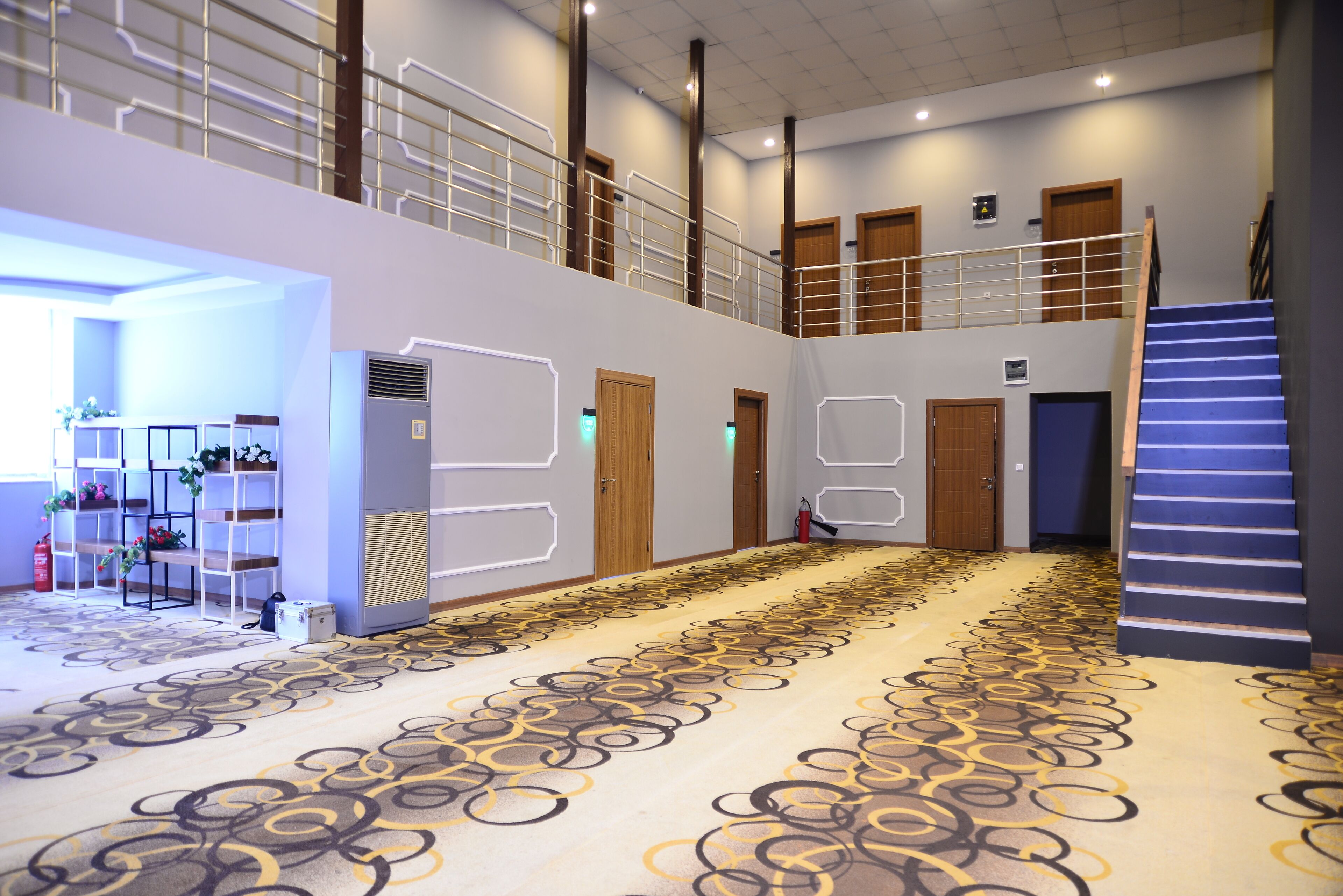 A spacious indoor area with a patterned carpet, a staircase, and a mezzanine level with railings.