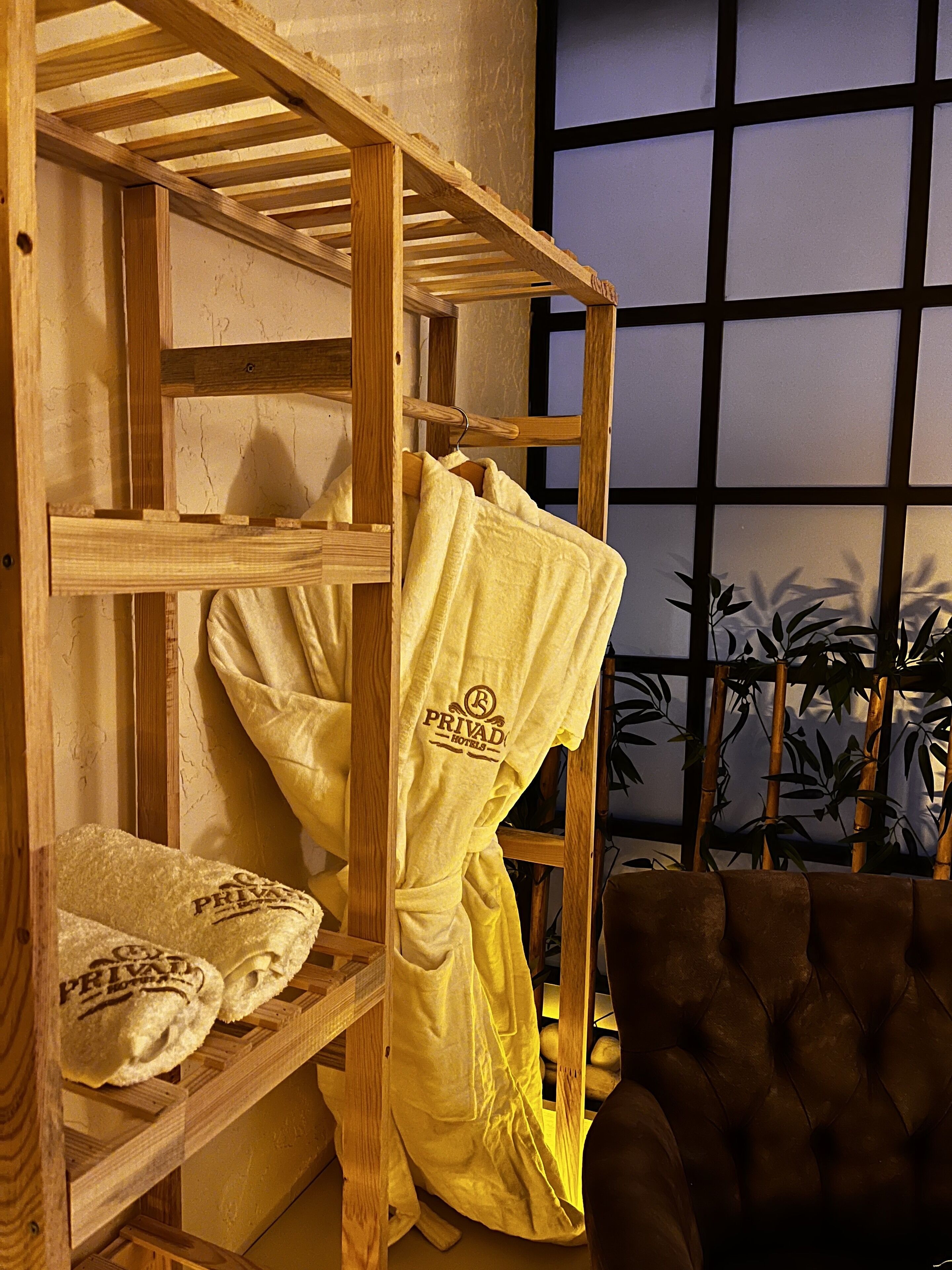A bunk bed with a yellow towel hanging on the side, a brown chair, and a window with a view of bamboo plants.